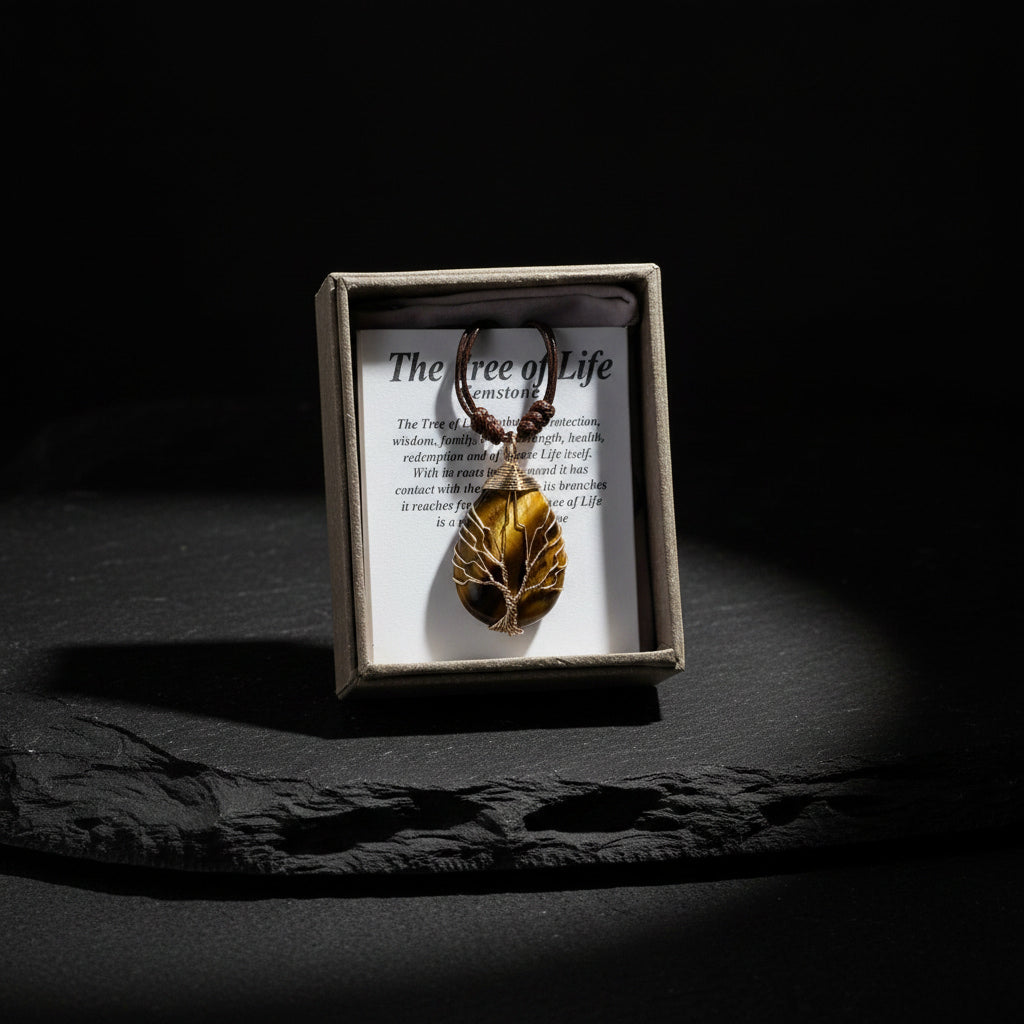 Leaf-shaped pendant in a box with 'The Tree of Life' text on a dark surface