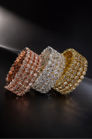 Three diamond-encrusted bangles in rose gold, white gold, and yellow gold on a dark background.