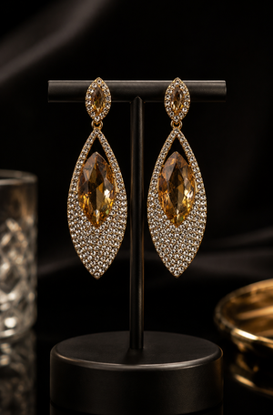 Pair of gold and crystal earrings on a black stand against a dark background
